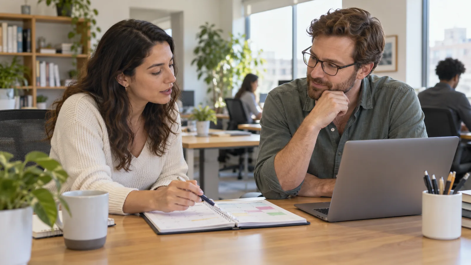 Dos compañeros conversan frente a un calendario de trabajo.